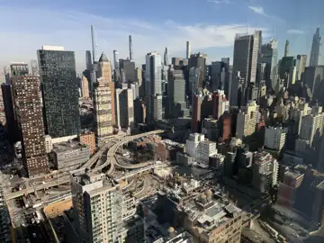 An aerial view of a dense New York City skyline with an elevated highway interchange, taken through a window.
