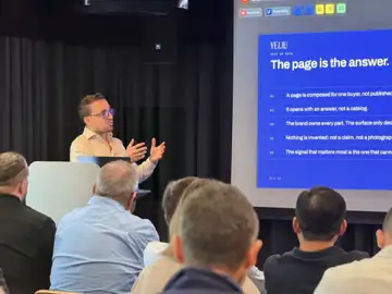 A man presents a slide titled 'The page is the answer' from Veliu to a seated audience, listing five points including 'A page is composed for one buye
